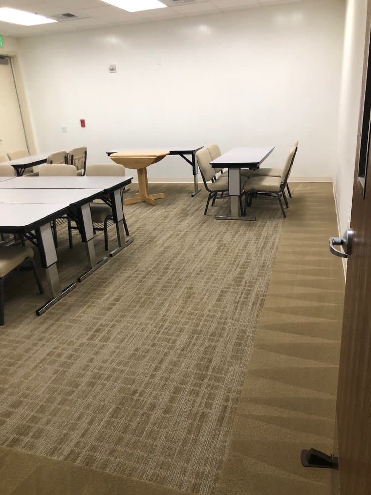 Corporate meeting room after a cleaning visit — tables squared, chairs pushed in, fresh vacuum lines in the carpet